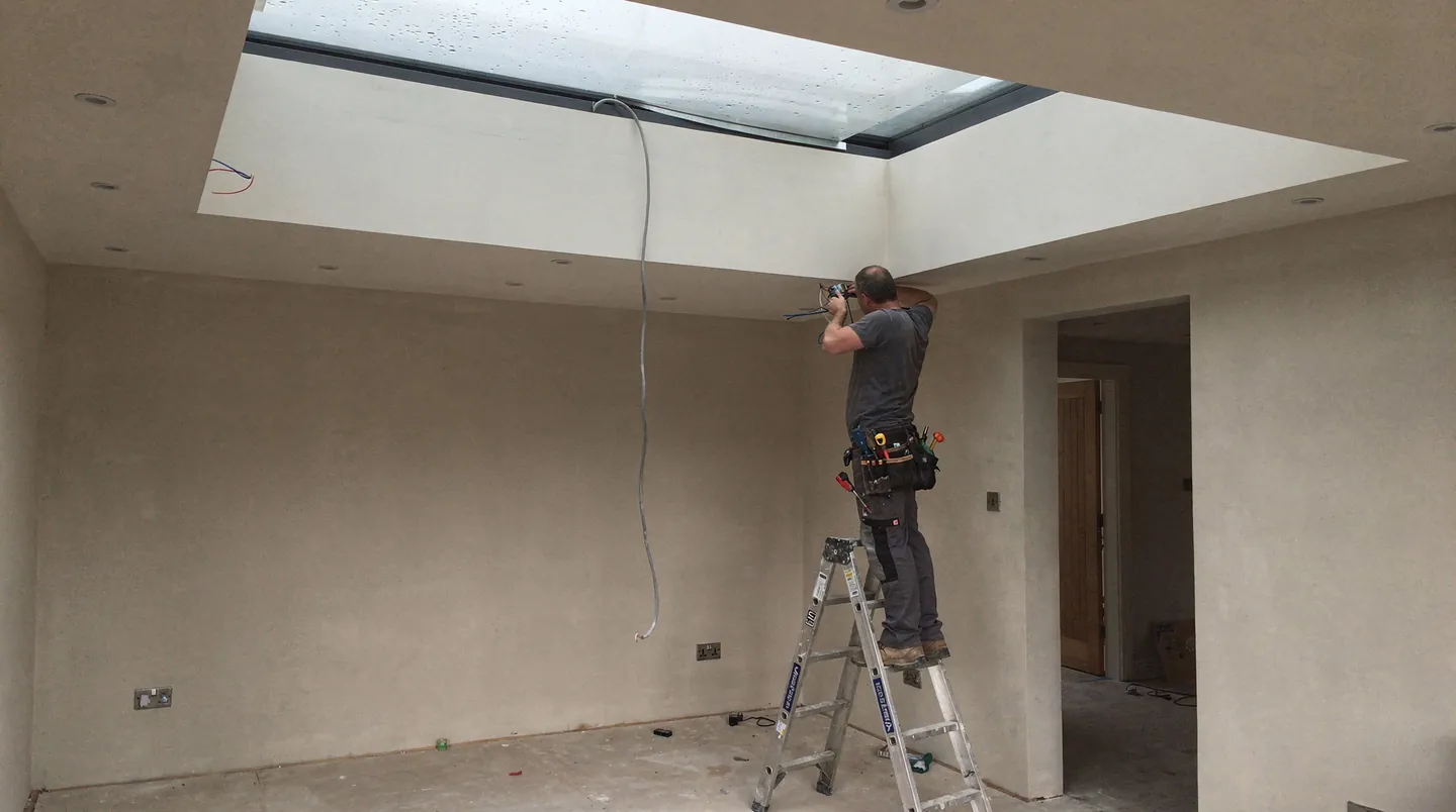 An electrician running cable between exposed joists in an extension before the ceiling is boarded