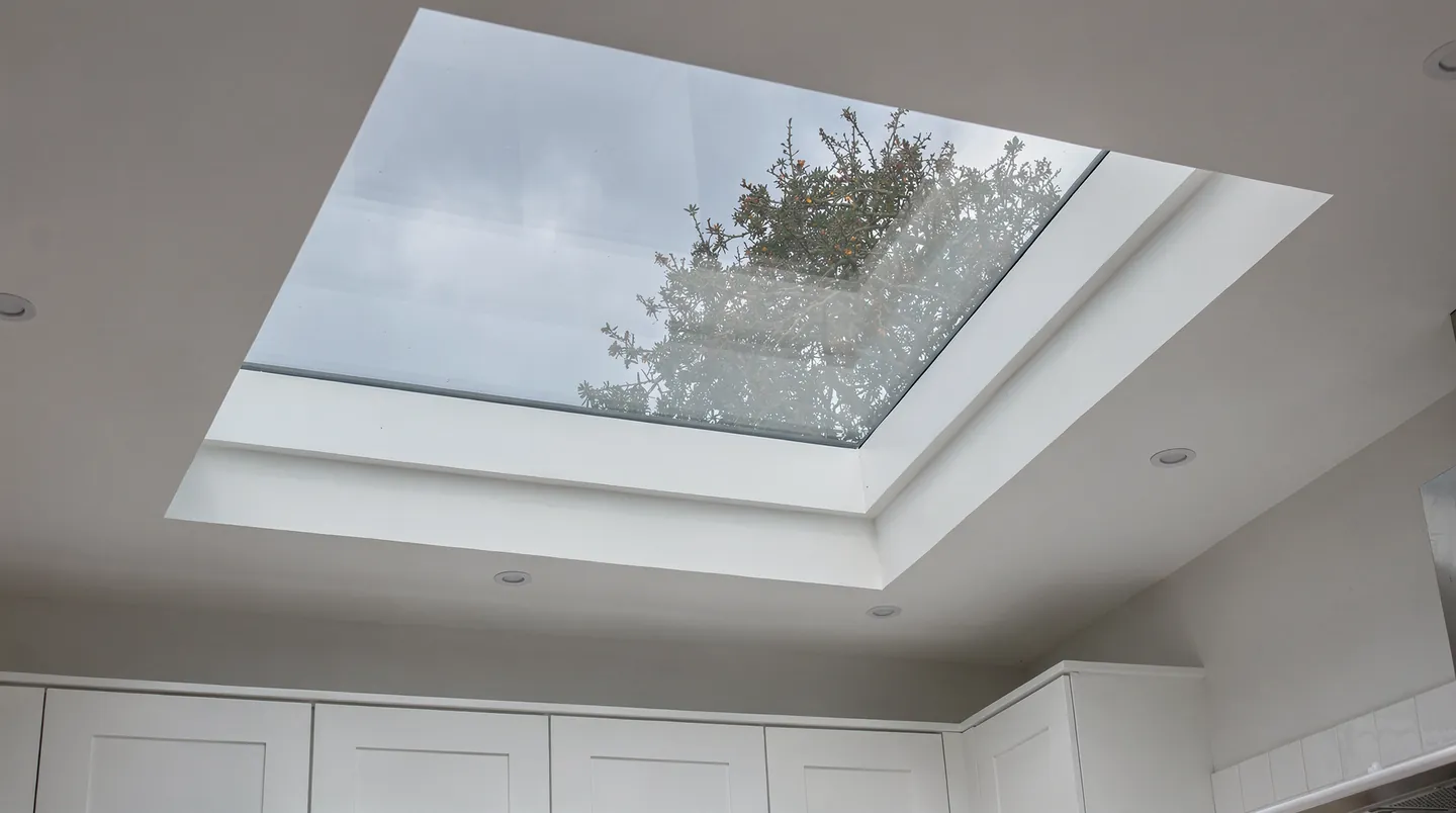 Blue sky and tree branches seen through a clear new rooflight above a kitchen