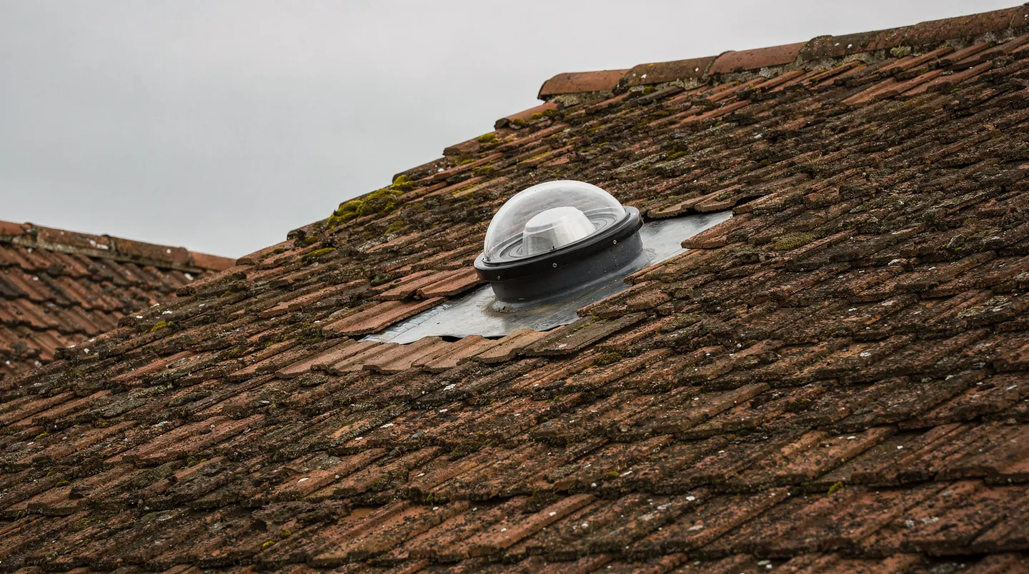 The clear round dome of a sun tunnel on a clay tile roof